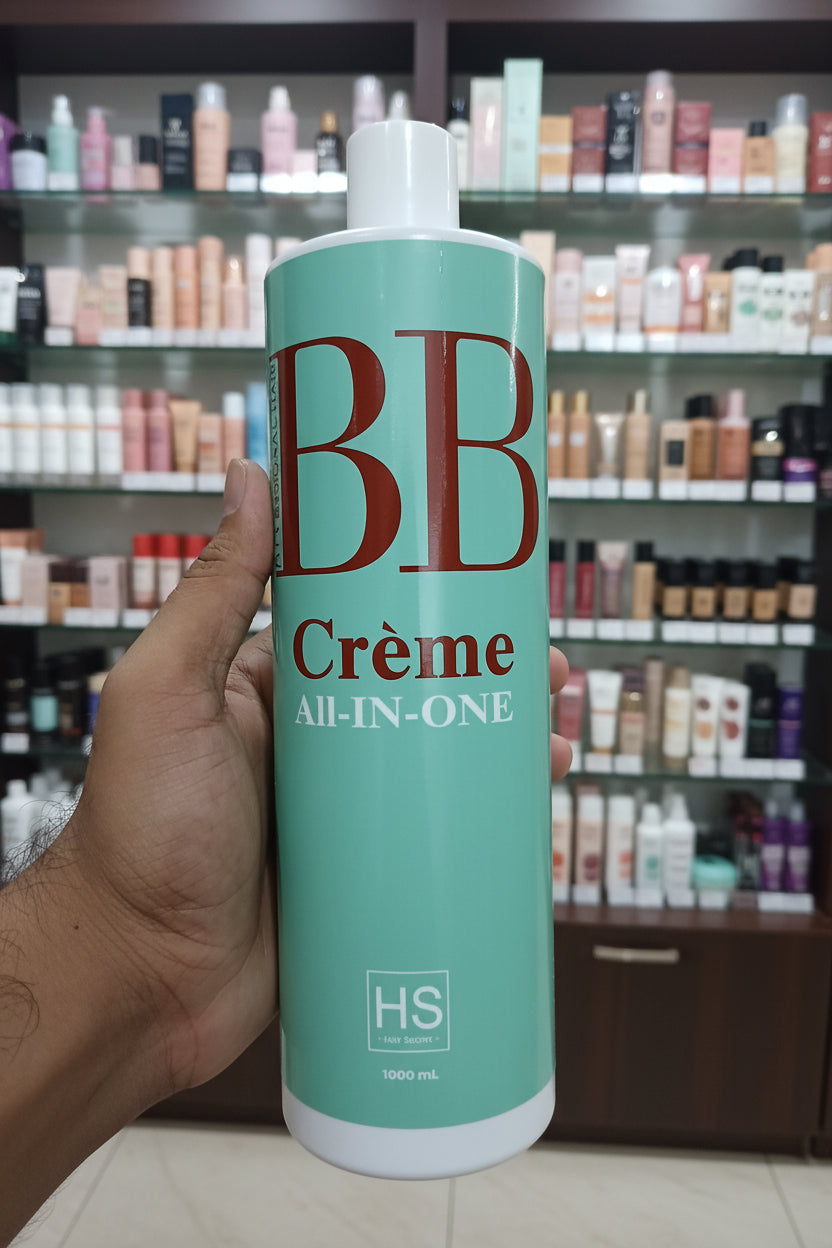A hand holding a mint green bottle of BB Crème All-In-One hair product against a speckled terrazzo tile background.